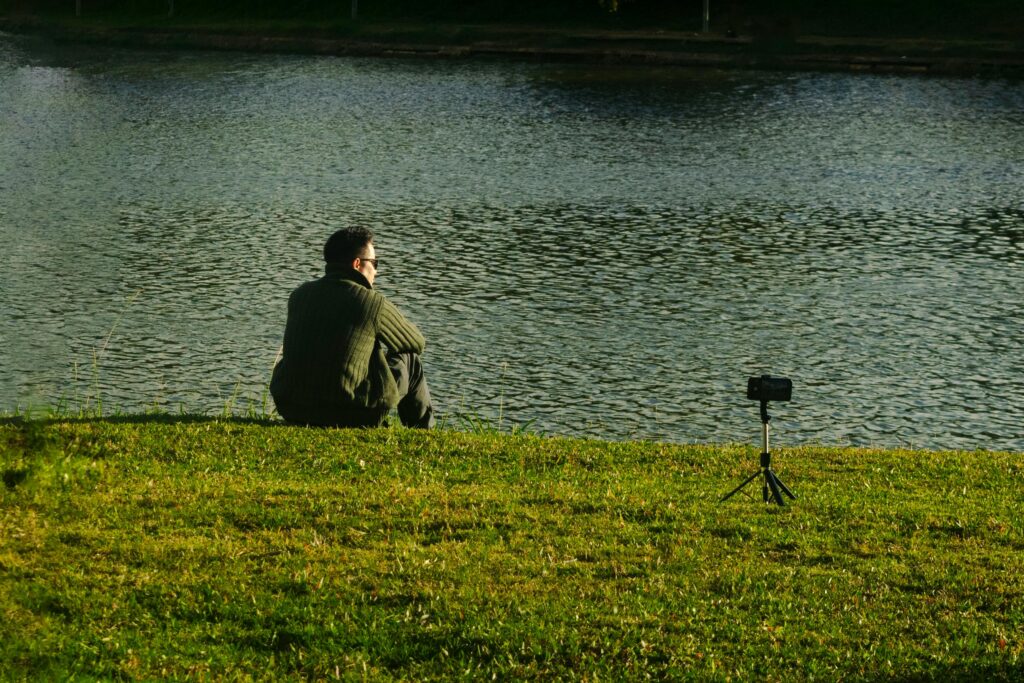 A man relaxes by a lake in Dalat, Vietnam, capturing the tranquil scenery with a camera.